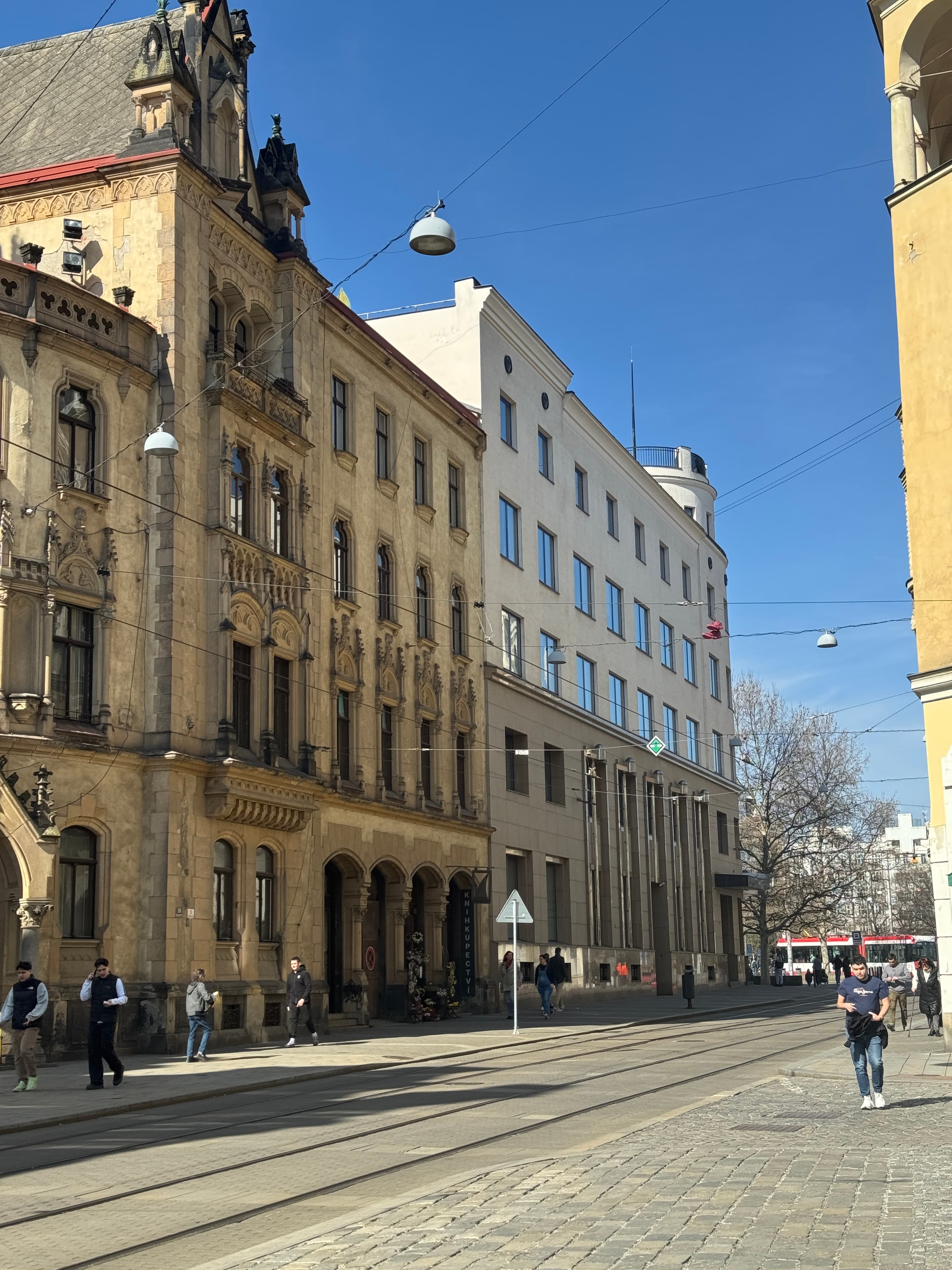 Ornate Neo-Gothic building facade on a sunlit street with tram tracks and pedestrians in Brno