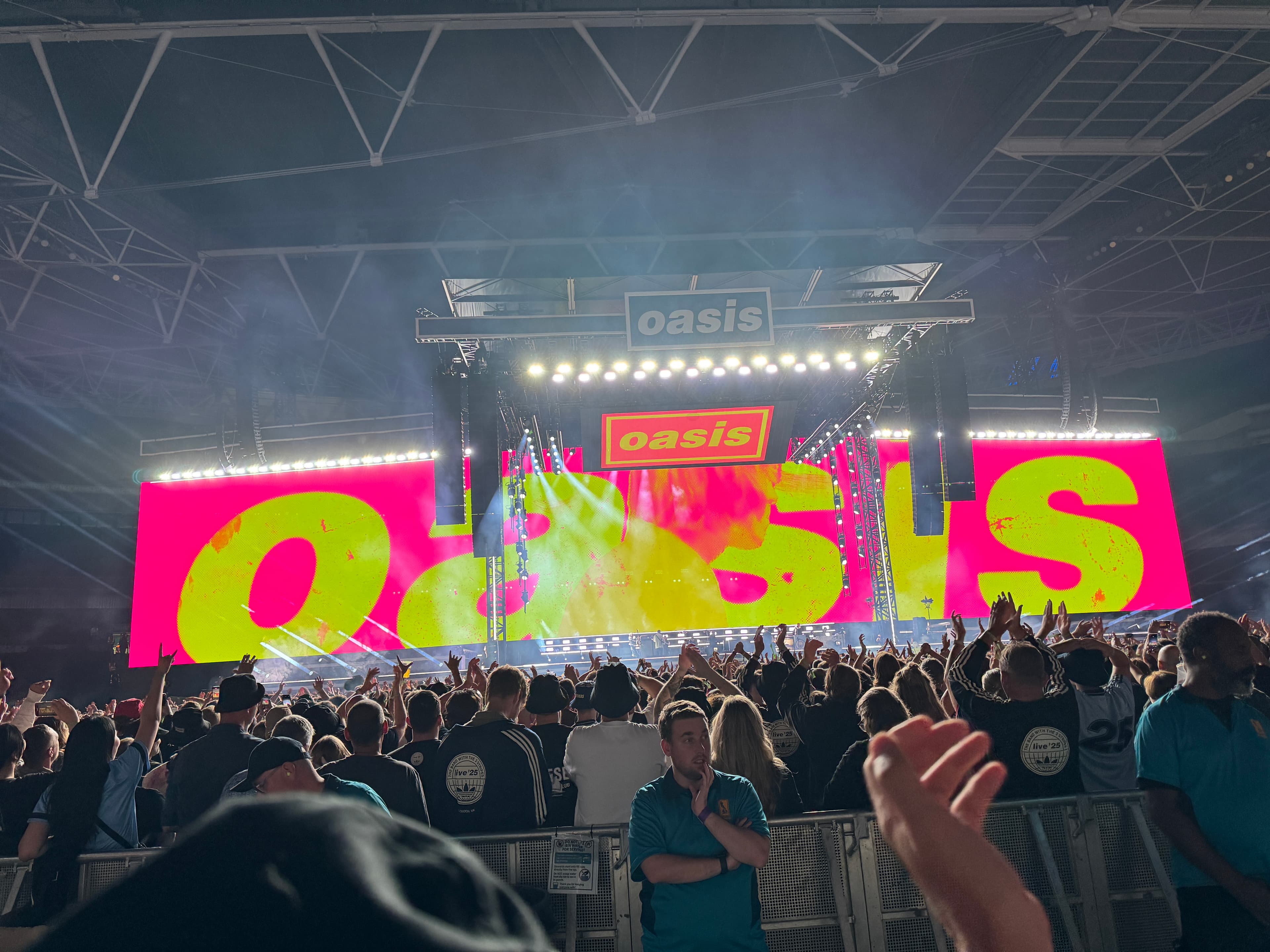 Oasis performing at Wembley Stadium, with a sea of fans in the background