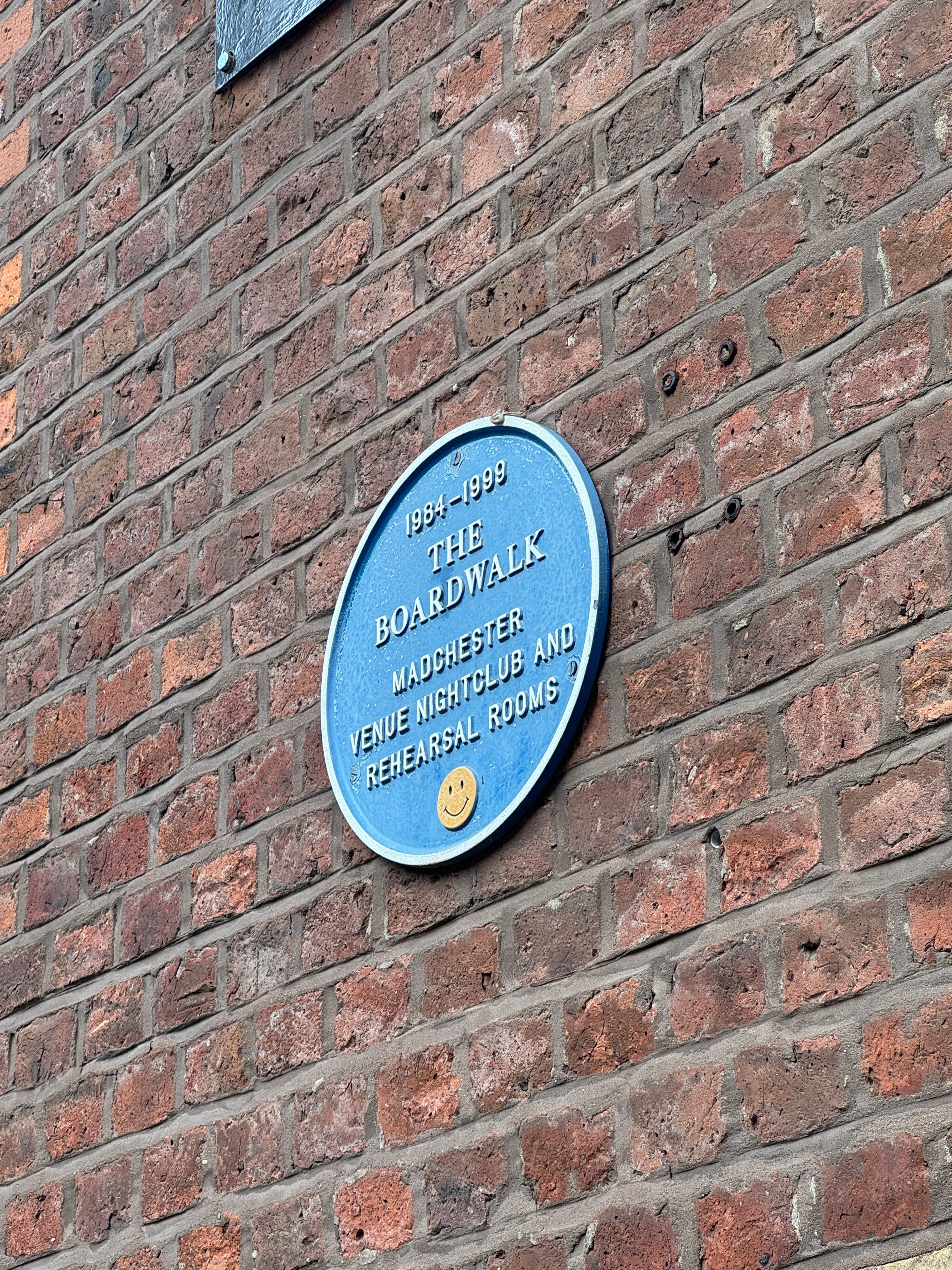 Blue heritage plaque mounted on a weathered red brick wall in Manchester
